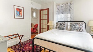 Un dormitorio con cama, una silla, un escritorio, una puerta y una ventana con cortinas.