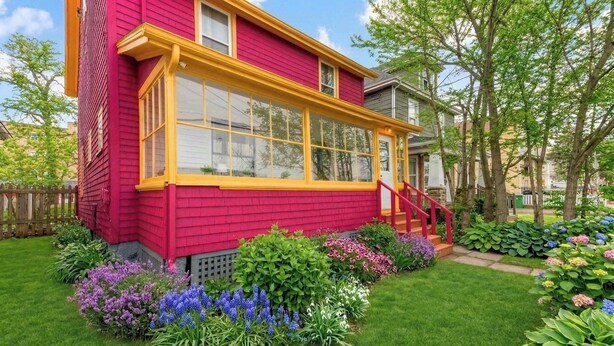 Una casa roja con detalles amarillos, un porche y un jardín con diversas flores.