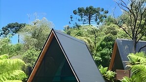 A modern, triangular-shaped cabin nestled among lush greenery, with a clear view of the surrounding forest. - Cabanas Lumberjack (Urubici)
