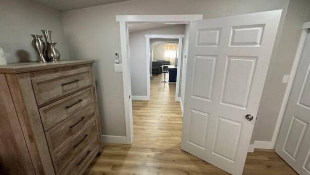 Um corredor com um aparador de madeira, uma porta branca e uma cozinha ao fundo.