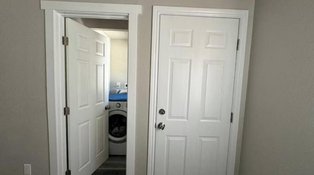A hallway with a closed door on the right and an open door leading to a laundry room.