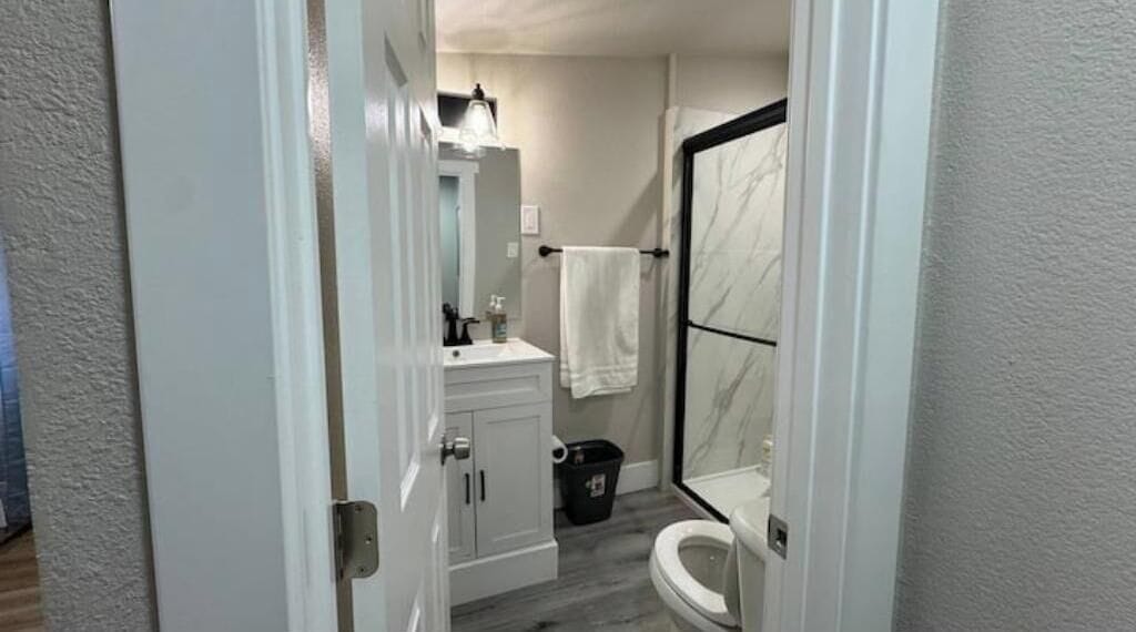 Un bagno con il water, un lavandino, uno specchio, un portasciugamani e una doccia con porta in vetro.