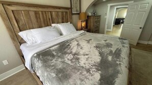 Quarto com cabeceira de madeira, cama com lençóis brancos e luminária em uma mesa de cabeceira.