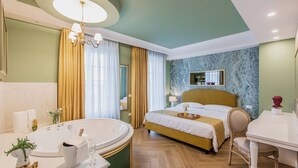 A hotel room with a large bathtub, a bed with a gold headboard, a wooden desk, and a marble-patterned wall. - Villa Oteri Room & Bistrot (Bacoli)