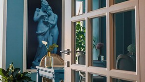 A room with a large blue statue on the wall, a door with glass panels, and a vase with a single flower on a table. - Villa Oteri Room & Bistrot (Bacoli)
