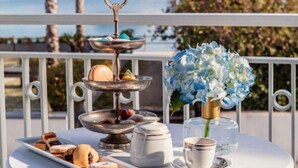 A table with pastries, a teapot, and a cup on a balcony with a view of a mountain and the sea. - Villa Oteri Room & Bistrot (Bacoli)