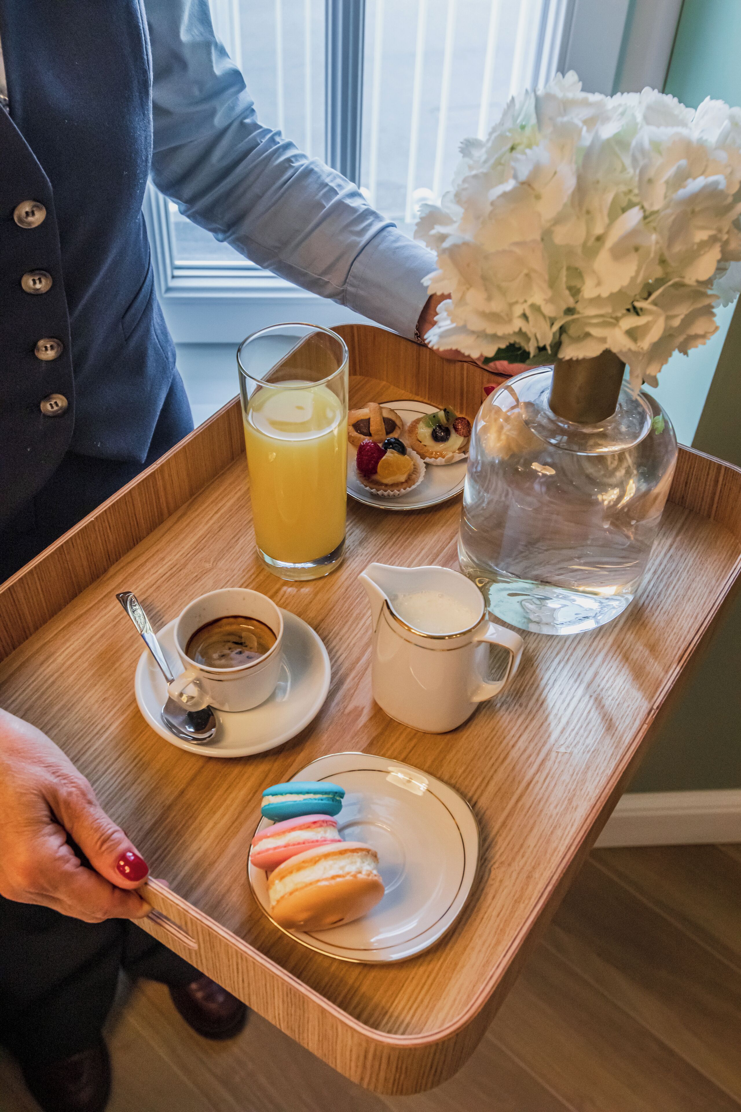 A tray with a glass of orange juice, a cup of coffee, a pitcher of water, macarons, and a small plate of pastries.