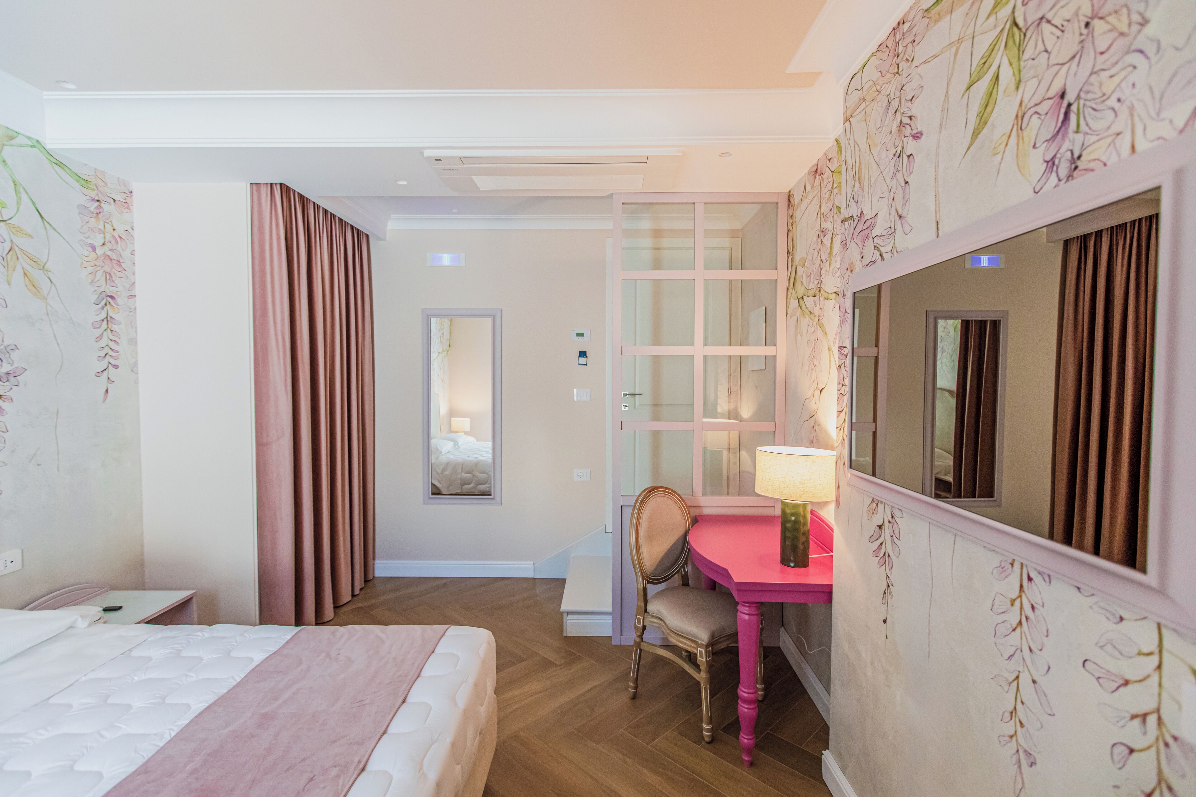 Une chambre d’hôtel avec un lit, un bureau et une chaise, un miroir et une fenêtre avec des rideaux.