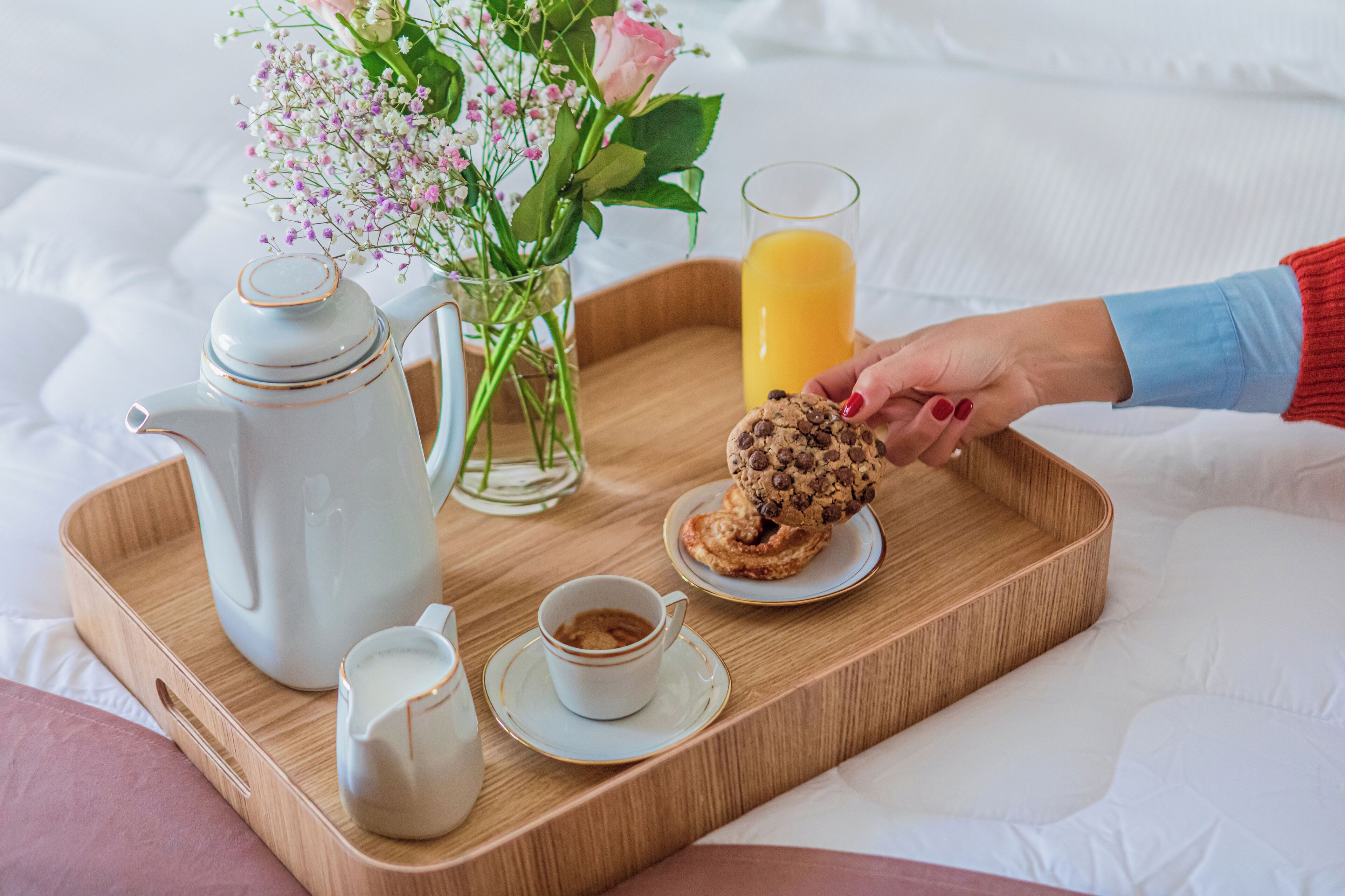 Ein Tablett mit Teekanne, einer Tasse Kaffee, einem Glas Orangensaft, einem Keks und einer Blumenvase.