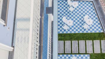 A rooftop pool area with checkered tiles, white lounge chairs, and a small patch of grass.