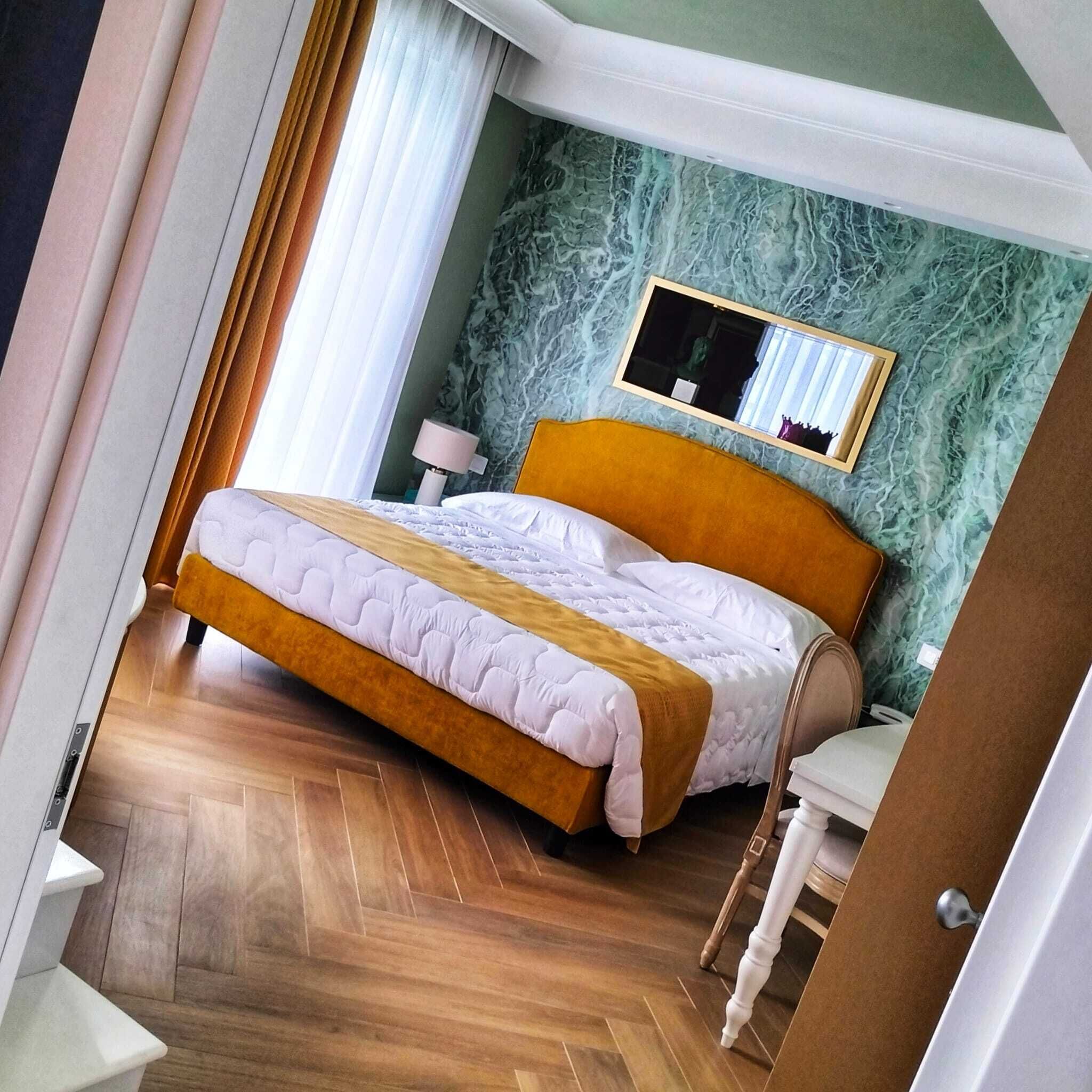 Een hotelkamer met een bed, nachtkastje, spiegel en een visgraatvloer.