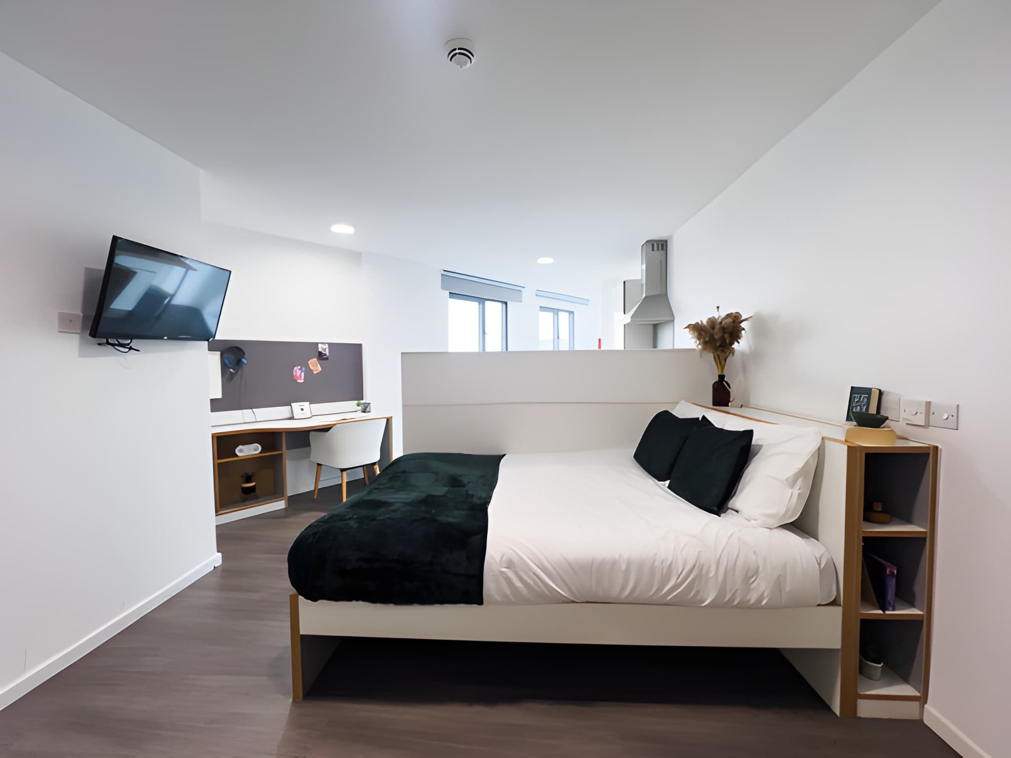 A modern bedroom with a bed, a desk, a chair, a TV, and a bookshelf.