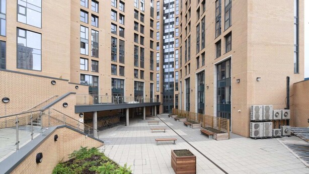 A multi-story building with a covered walkway, outdoor seating, and air conditioning units. - For Students Only Cosy Ensuite Rooms With Private Bathrooms at Dobbie's Point in Glasgow (Glasgow)