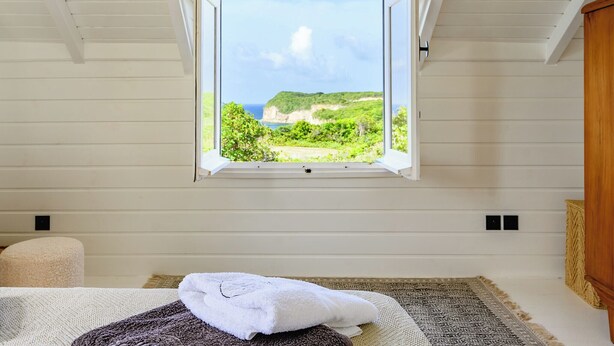 A bedroom with a large window overlooking a coastal landscape. - Villa Calypso a charming retreat with a saltwater pool and sea views (Saint-Louis)