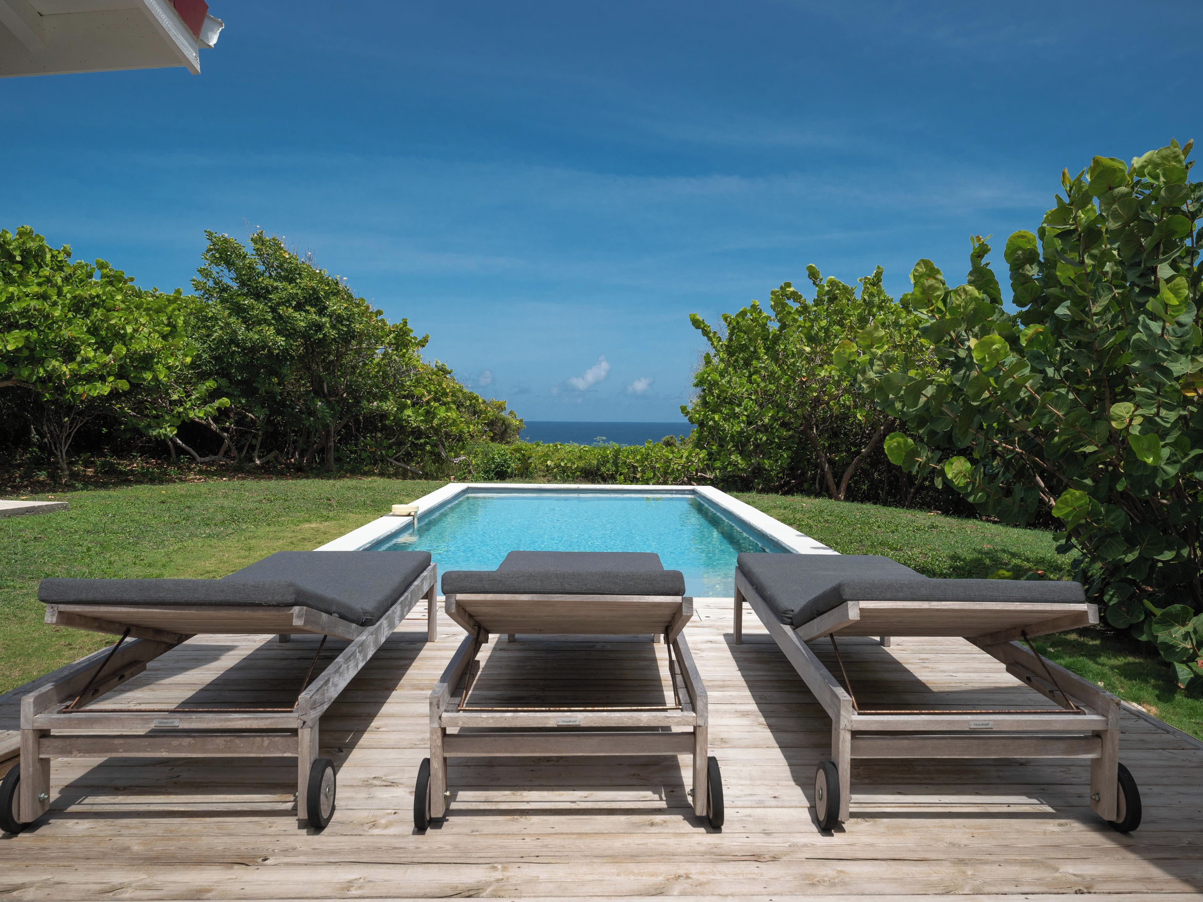 Une piscine avec trois chaises longues donnant sur l’océan.