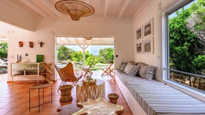 A spacious living area with a large window, a sofa, a dining table, and a decorative chair. - Villa Calypso a charming retreat with a saltwater pool and sea views (Saint-Louis)