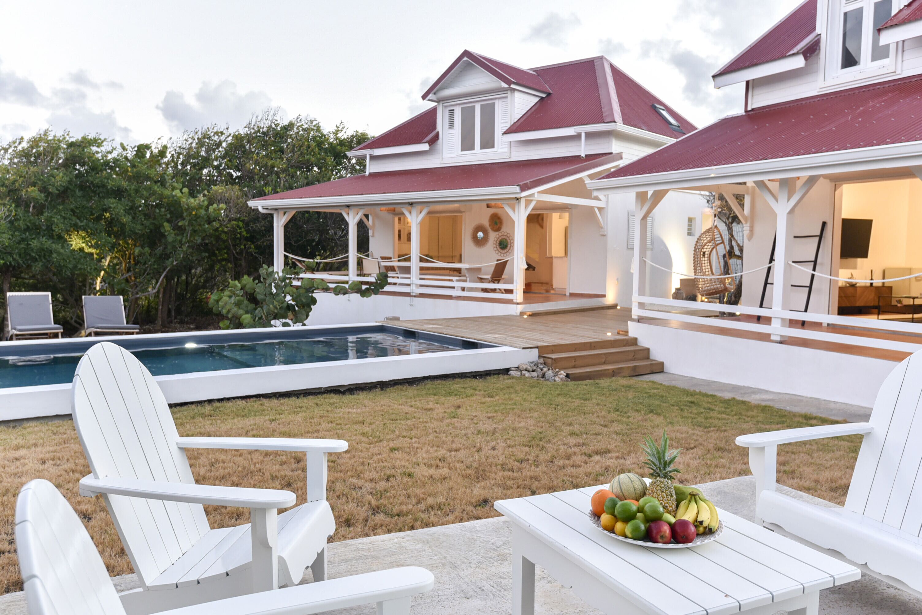 Ein zweistöckiges Haus mit Swimmingpool, Sitzgelegenheiten im Freien und einer Obstschale auf einem Tisch.
