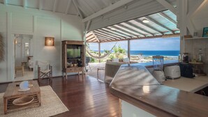 Ein geräumiger Wohnbereich mit Holzboden, einem Fernseher und einer Hängematte mit Blick auf eine malerische Meerlandschaft.