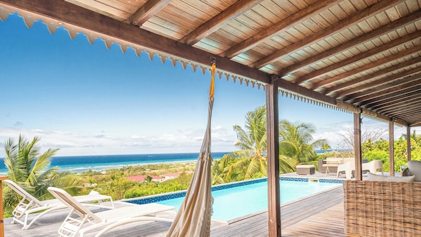 Eine Holzterrasse mit einer Hängematte, Liegestühlen und einem Pool mit Blick auf einen Strand.