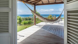 Ein offenes Durchgang zu einer Holzterrasse mit einer Hängematte und Blick auf den Ozean.