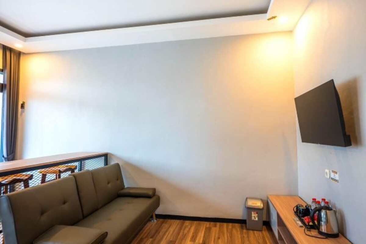 Una sala moderna con un sofá, un televisor montado en la pared, una mesita con un hervidor y una ventana con cortinas.