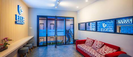 A hotel reception area with a red sofa, a reception desk, and a glass door leading to a staircase.
