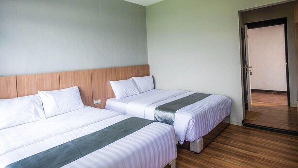 Habitación de hotel con dos camas, suelo de madera y una puerta que da a otra habitación.