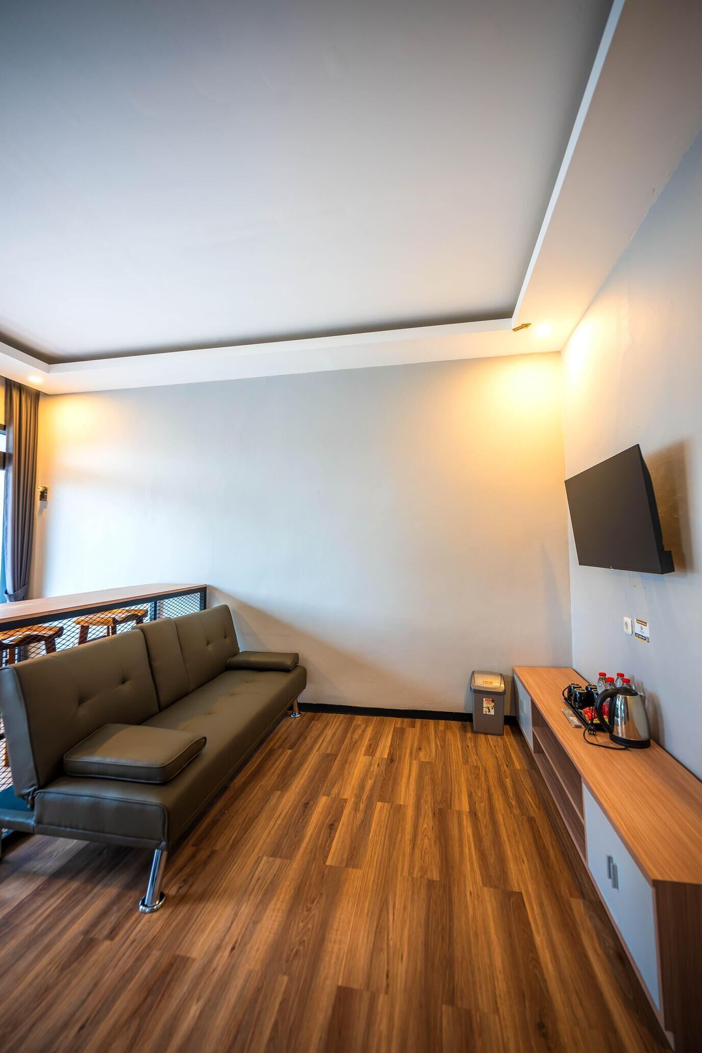 A modern living room with a sofa, wooden flooring, a TV mounted on the wall, and a small table with bottles.