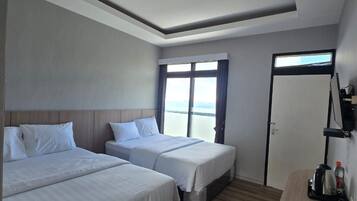 Habitación de hotel con dos camas individuales, piso de madera, un ventanal grande con cortinas y una zona de kitchenette.
