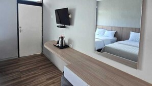 Habitación de hotel moderna con piso de madera, cama grande con ropa de cama blanca, mesita de noche con cafetera, televisor de pantalla plana montado en la pared y puerta con marco negro.