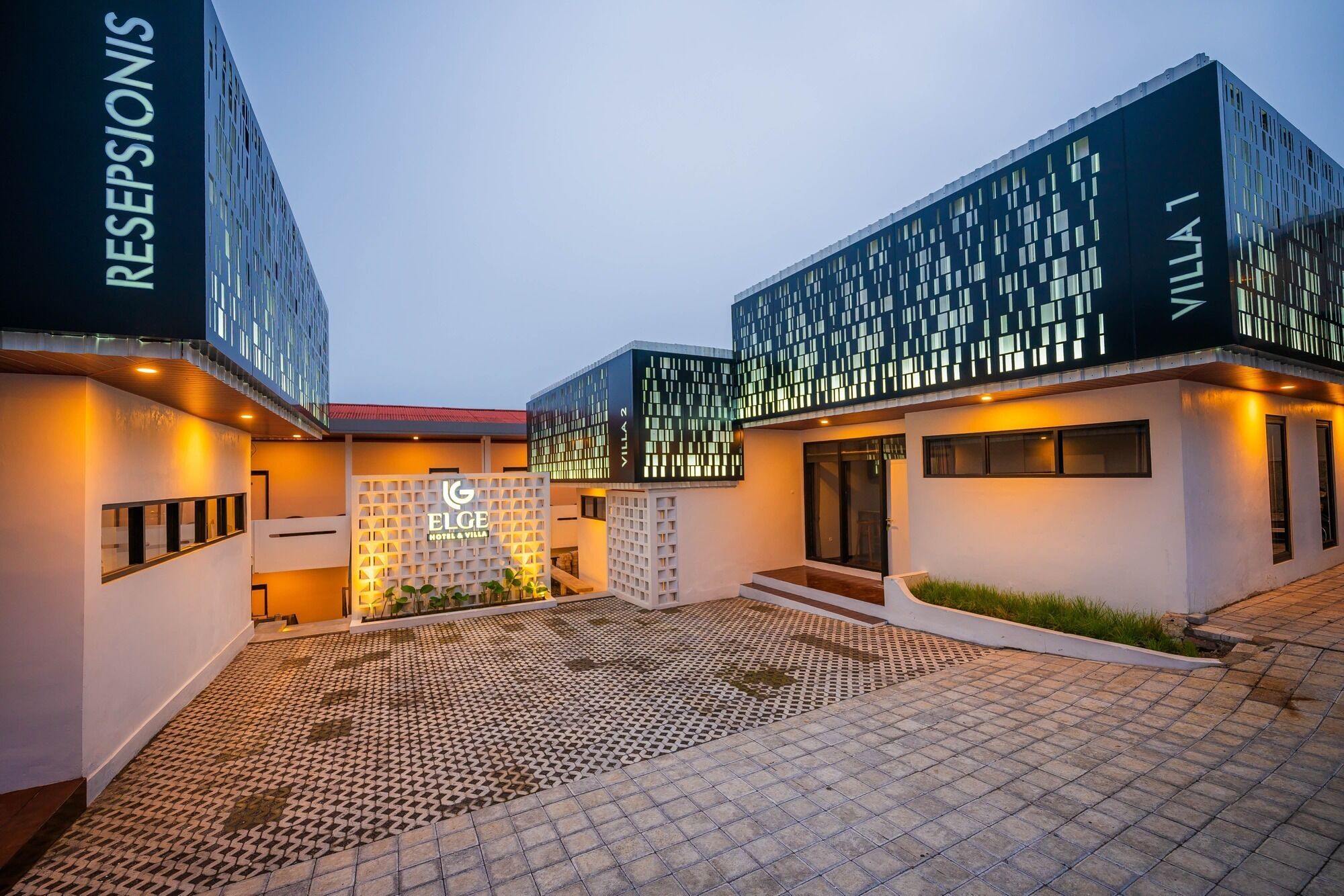 Un hôtel moderne doté d’un hall d’accueil, d’une enseigne indiquant « ELGE HOTEL & VILLA », et d’une cour dallée.