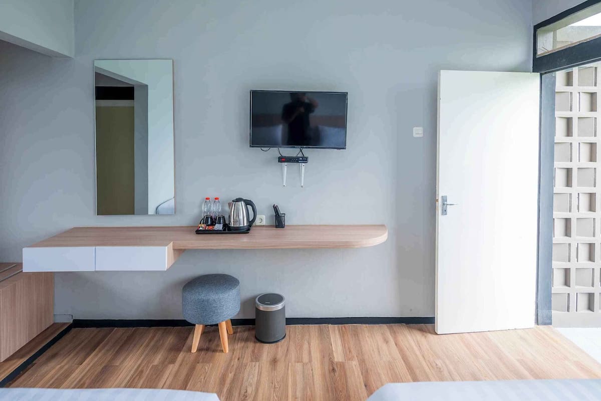 A modern hotel room with a flat-screen TV mounted on the wall, a wooden desk with a mirror, a small seating area, and two beds.