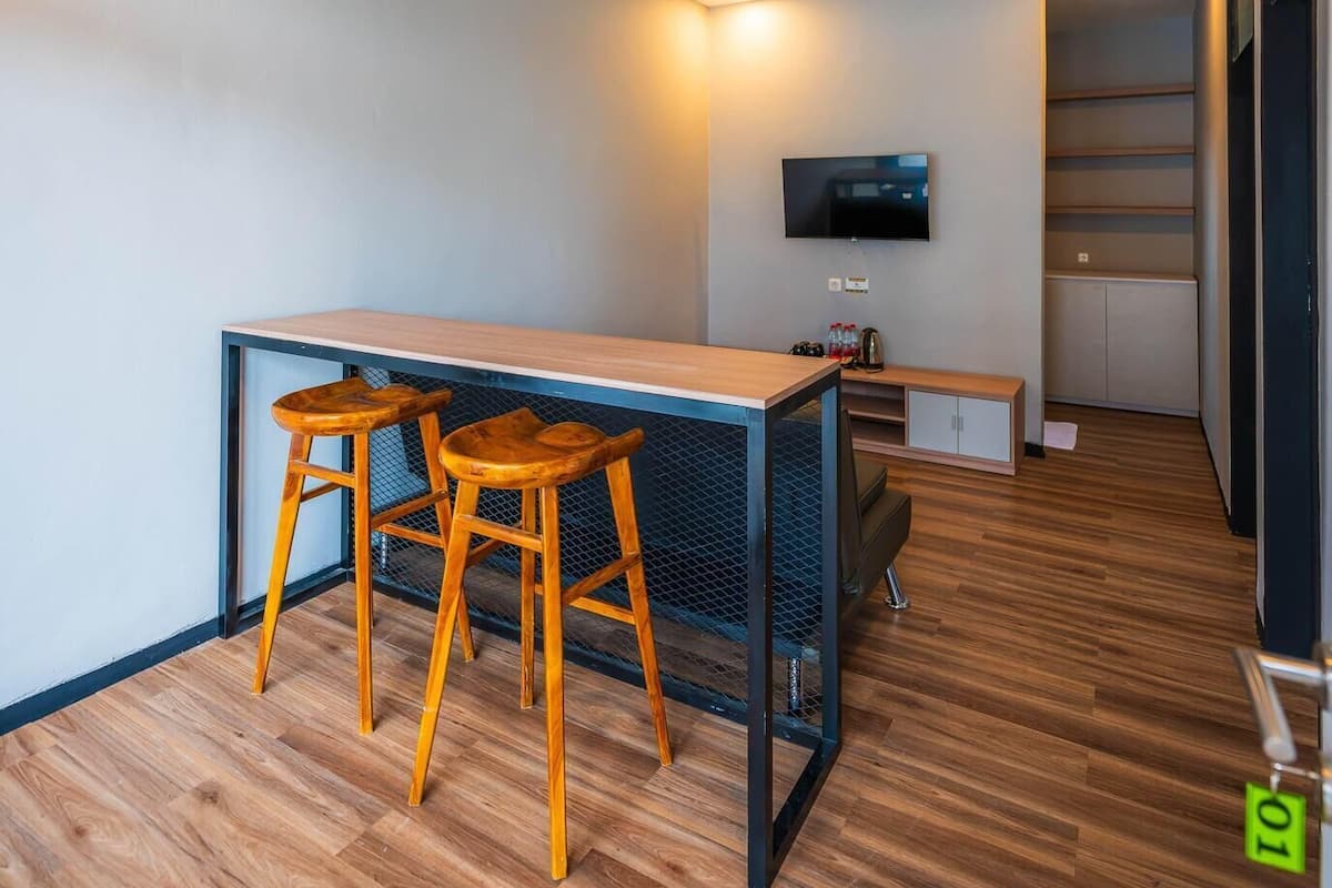 A modern kitchen with a wooden countertop, two stools, a TV mounted on the wall, and a staircase leading to an upper level.