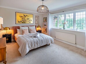 A bedroom with a large bed, two bedside tables with lamps, a window with a view of greenery, and a ceiling light fixture.