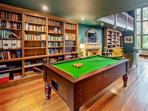 Uma biblioteca com mesa de bilhar, estantes de madeira e lareira.