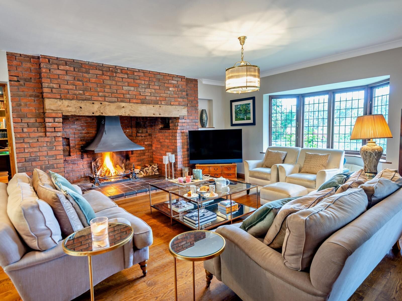 A living room with a brick fireplace, comfortable seating, a television, and a large window.