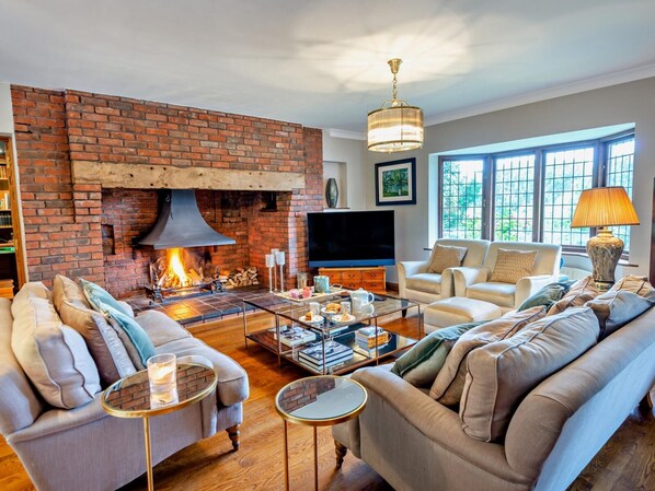 A living room with a brick fireplace, comfortable seating, a television, and a large window.