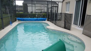 A swimming pool with a green chair, a covered patio area, and a house in the background.