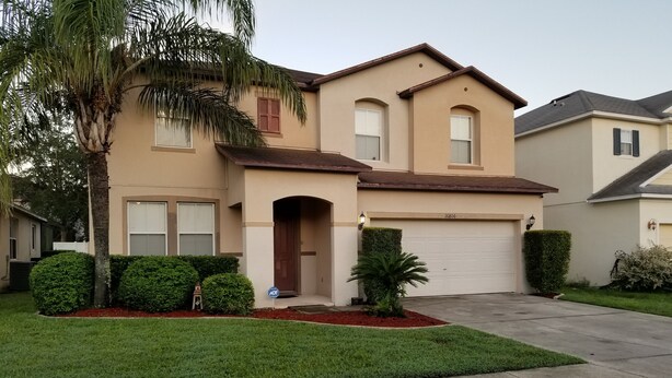 A two-story house with a beige exterior, a front entrance with a brown door, and a garage.