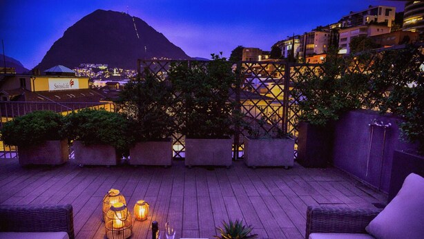 A rooftop terrace with wicker furniture, potted plants, and lanterns. - Luxury Nassa Penthouse With Private Terrace in Lugano (Lugano)