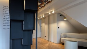 A modern interior with a wooden floor, a grey sofa, a white cylindrical object, and a wall with text. - BHB Boutique House (Macedo de Cavaleiros)
