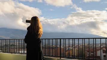 Una persona tomando una foto con un teléfono inteligente, con vistas a un paisaje urbano que incluye edificios y montañas al fondo.