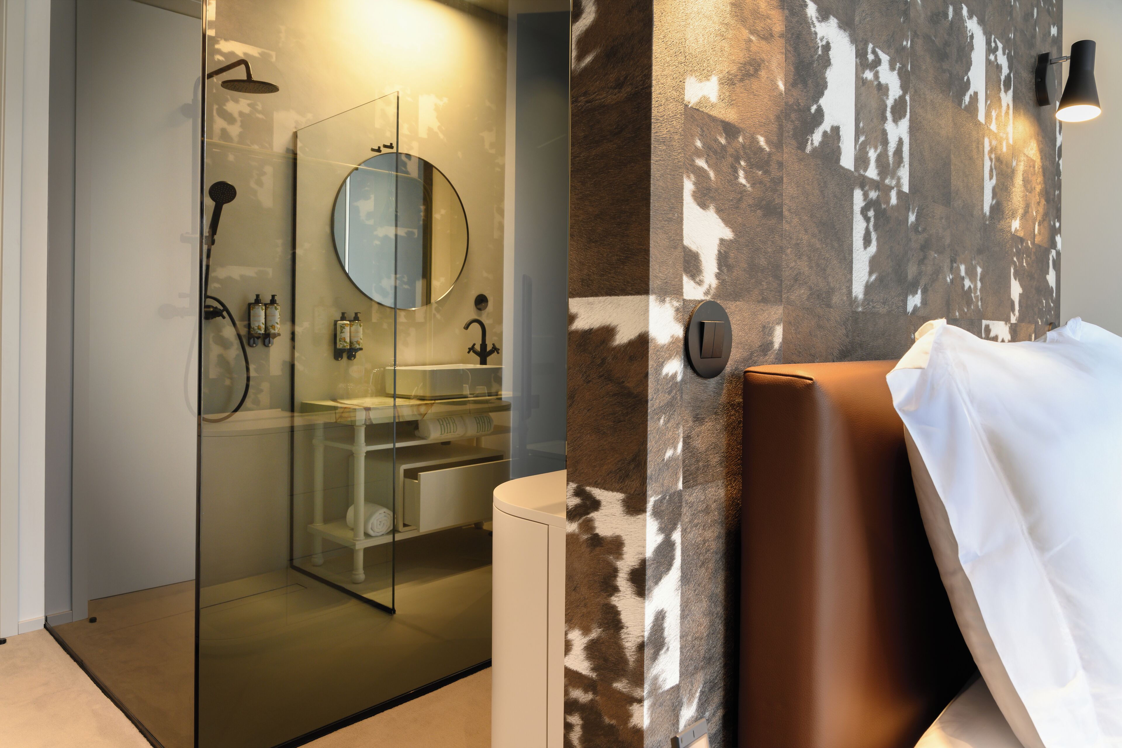 A modern bathroom with a glass-enclosed shower, a round mirror, and a white sink.