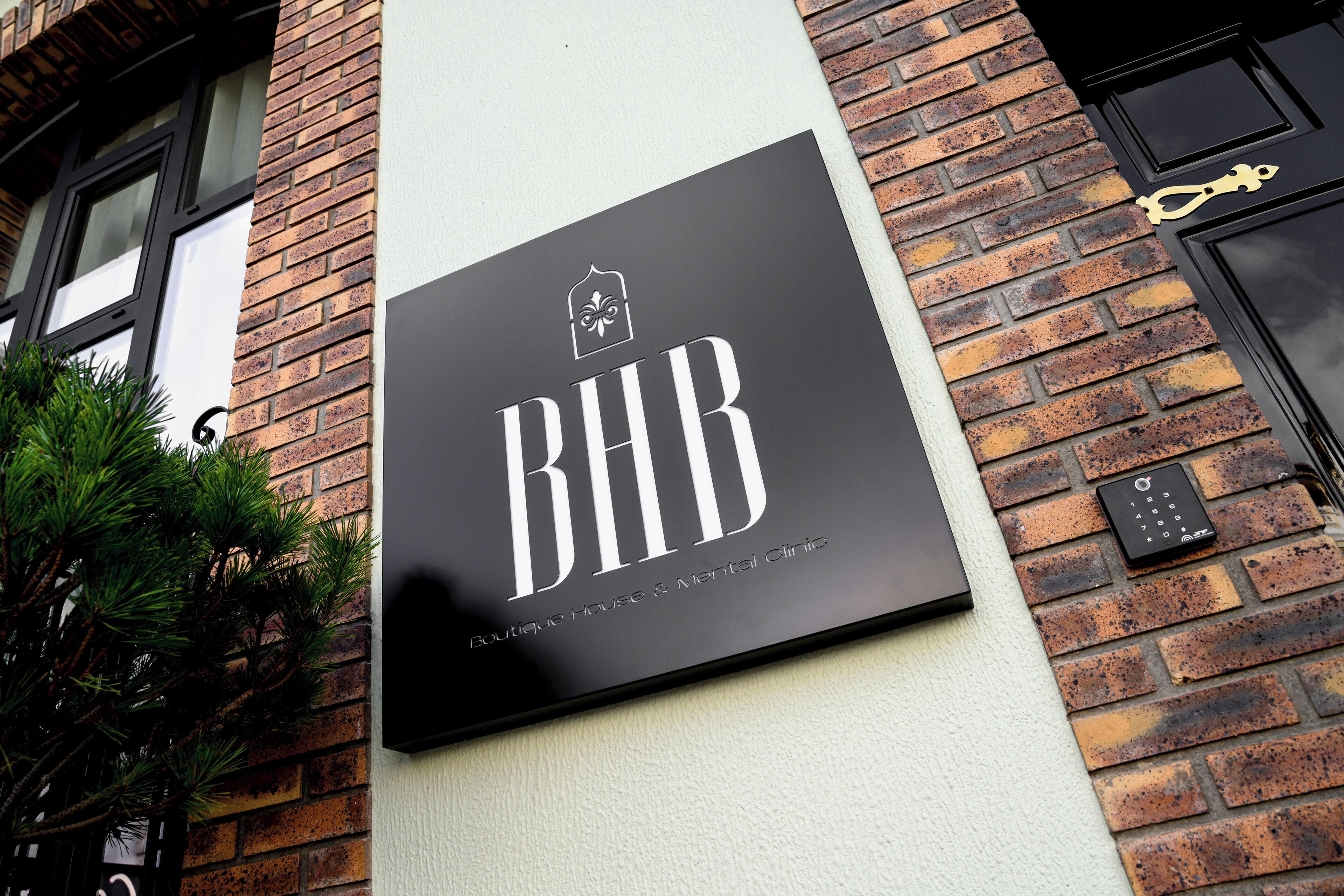 Un letrero negro con letras blancas que dice 'BHB Boutique House & Mental Clinic' sujeto a una pared de ladrillo.