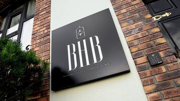 Un letrero negro con letras blancas que dice 'BHB Boutique House & Mental Clinic' sujeto a una pared de ladrillo.