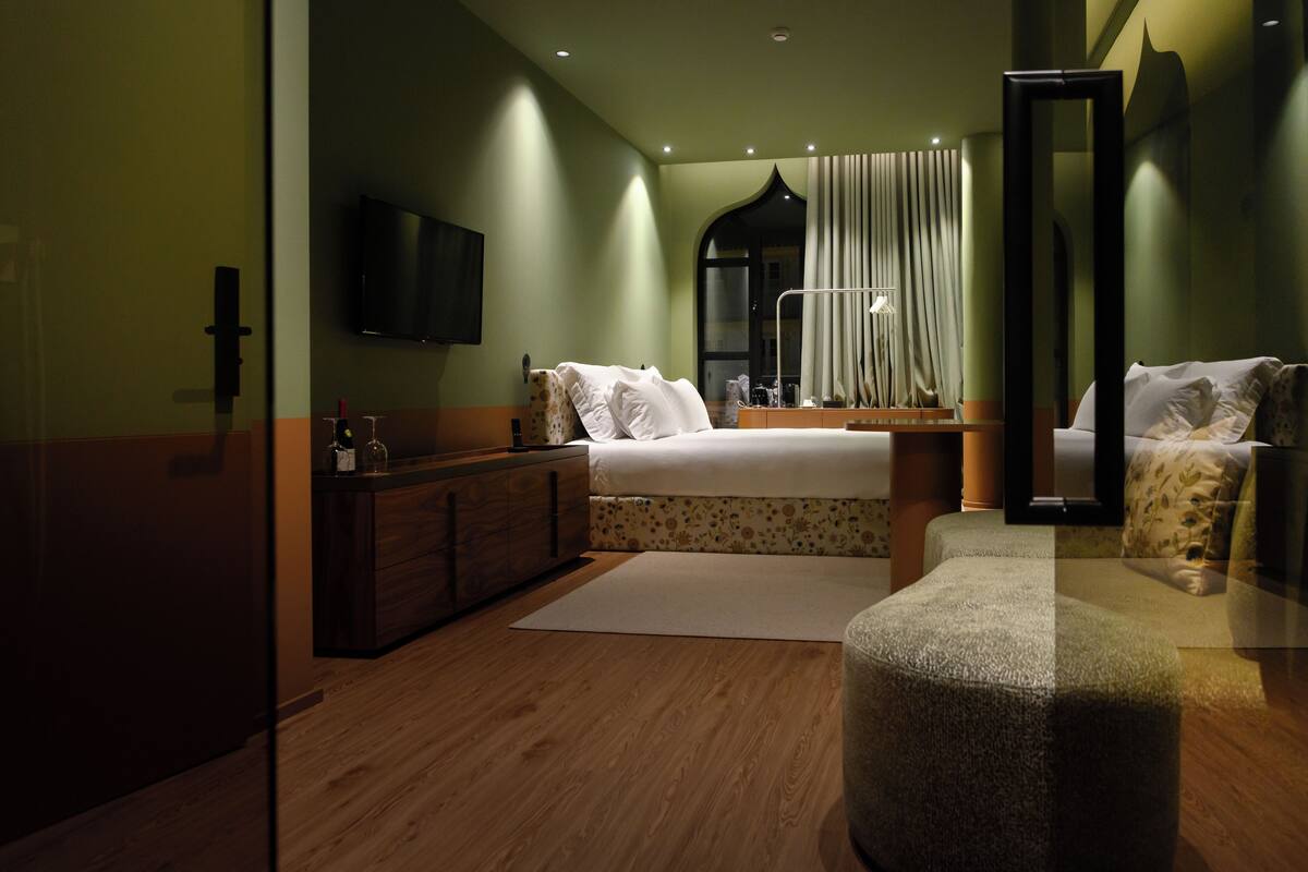 A modern hotel room with a large bed, a dresser, a mirror, and a flat-screen TV.