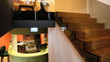 Un interior moderno con una escalera de madera, un mostrador de recepción y una zona de estar con sillas.