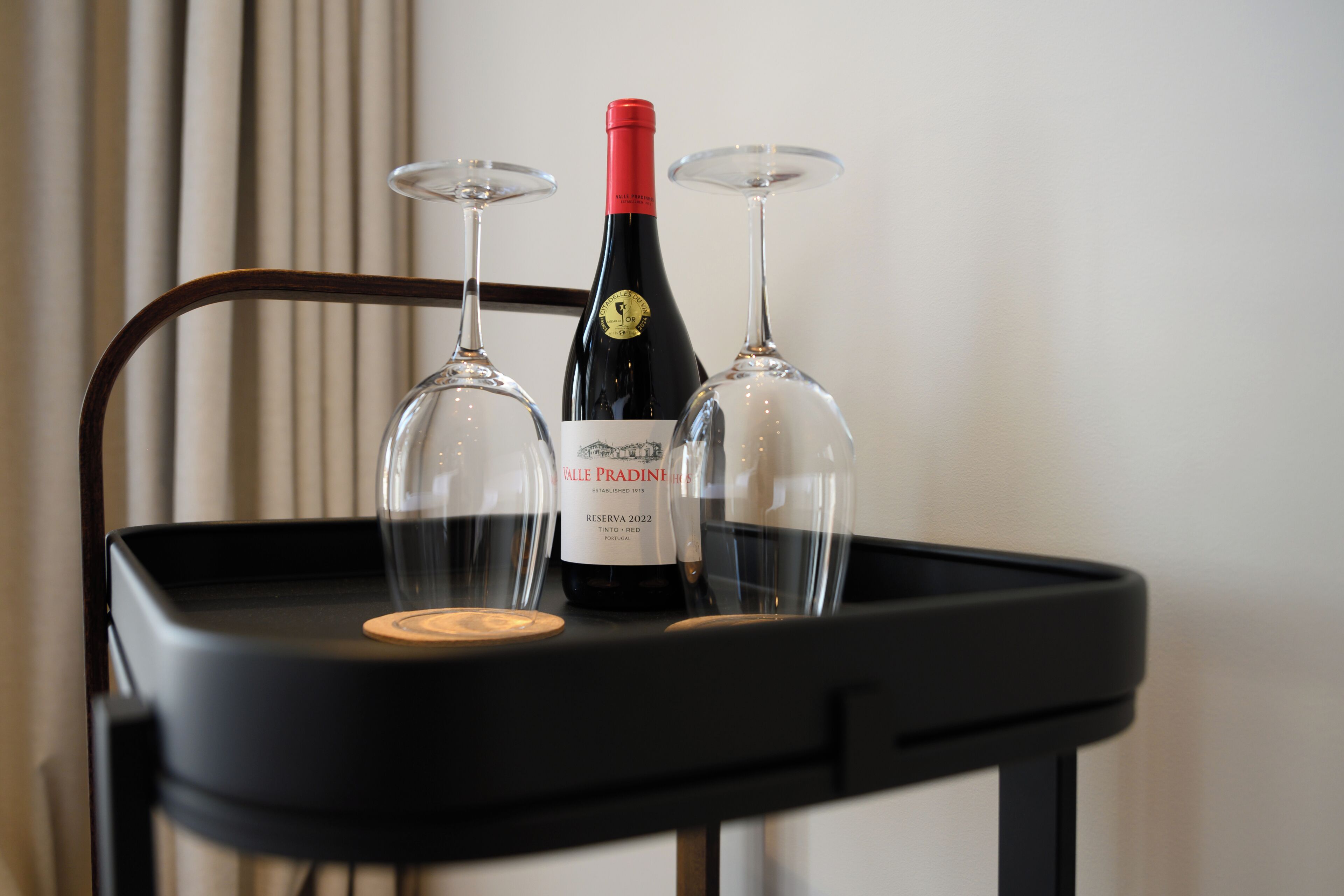 Una bandeja negra con una botella de vino y dos copas de vino sobre una silla.