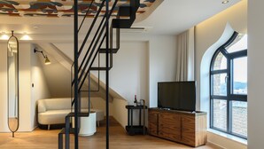 A modern hotel room with a wooden floor, a sofa, a TV, a staircase, and a large window. - BHB Boutique House (Macedo de Cavaleiros)
