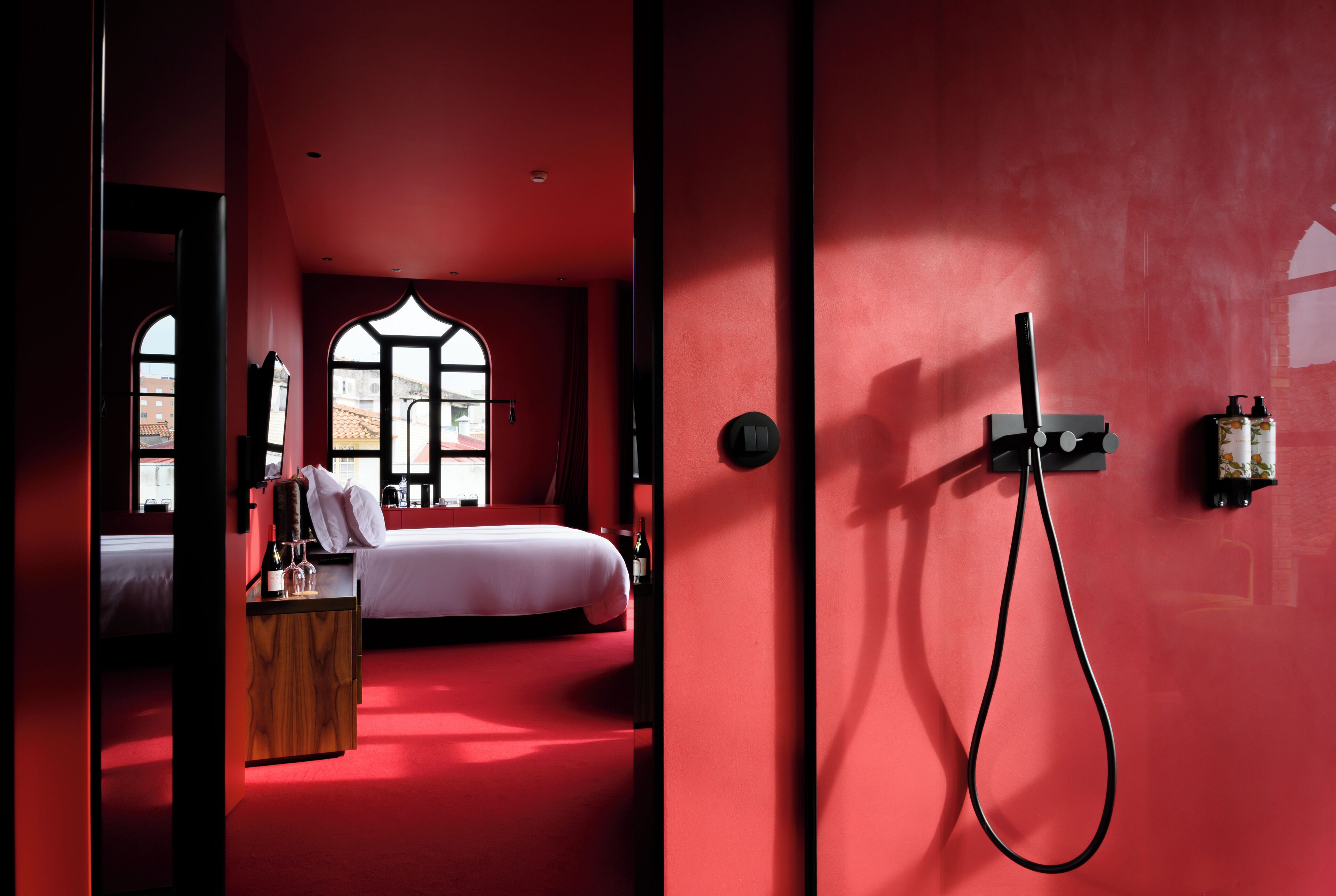 Una stanza dalle pareti rosse con un letto, un armadietto in legno e una doccia.